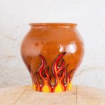 Ročno izdelan terra cotta cvetlični lonec z motivom ognjenih plamenov v pop-art stilu, v odtenkih rdeče, rumene in oranžne.