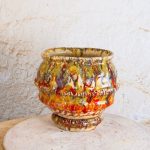Ročno izdelan cvetlični lonec Ignis s podstavkom, narejen s tehniko kačic iz bele in terra cotta gline, z živahnimi prelivi glazur v ognjenih oranžnih, rumenih in rjavih tonih.