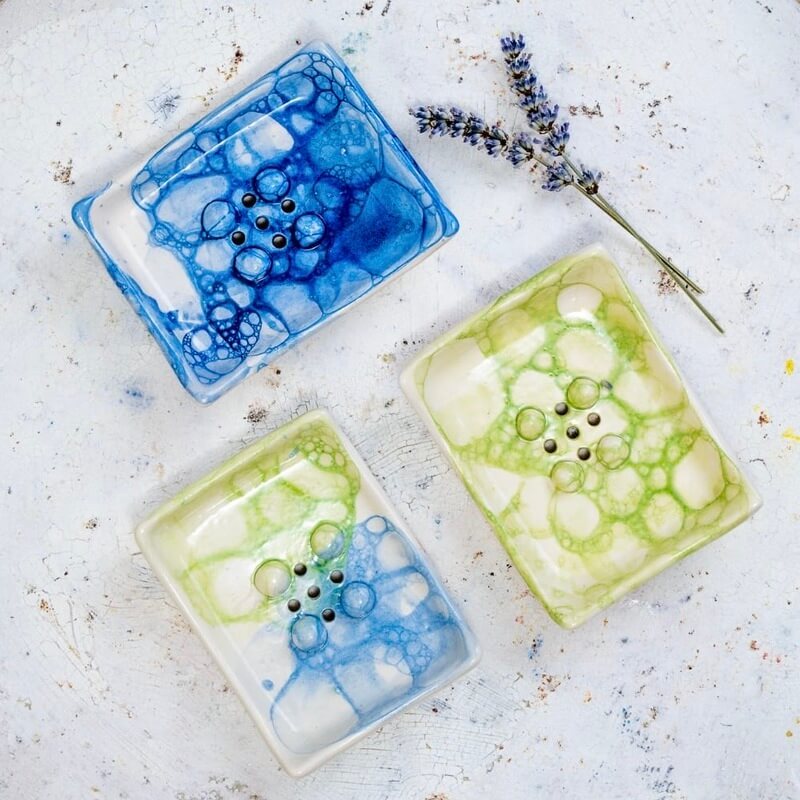 Ročno izdelan pravokotni keramični milnik iz bele gline, dekoriran s tehniko mehurčkanja v svežih modrih in zelenih tonih. Gumbi in odtočne luknjice ohranjajo milo suho, mehurčkast vzorec pa doda kopalnici igriv, peneč značaj.