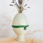 Jajčasta keramična vaza iz bele gline v tehniki kačic, z zelenim pasom na sredini; primerna za sveže ali suho cvetje.
